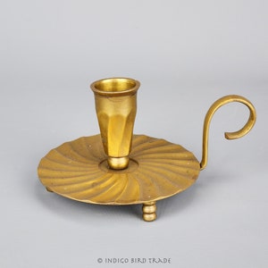 Puede incluir: Un candelero de metal dorado con una base en espiral y un solo portavelas. El candelero tiene un asa curva.