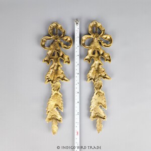 May include: Two gold-toned metal decorative pieces with a floral design. Each piece features a bow at the top and a series of cascading leaves.