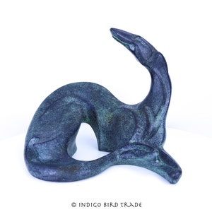 May include: A dark green ceramic sculpture of a stylized dog lying down with its head turned to the side. The sculpture has a smooth, polished finish.