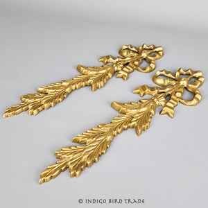 May include: Two gold-toned metal decorative pieces with a leafy design and a bow at the top.