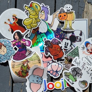 Könnte beinhalten: Eine Sammlung bunter Aufkleber mit verschiedenen Comicfiguren, darunter eine Schlange, ein Kürbis, ein Zwerg, eine Disney-Figur und ein Comic-Elefant. Die Aufkleber befinden sich auf einer grauen Holzoberfläche. Der Text auf den Aufklebern lautet "Let's Have This Sticker!" und "Ain't This Juse the Way".