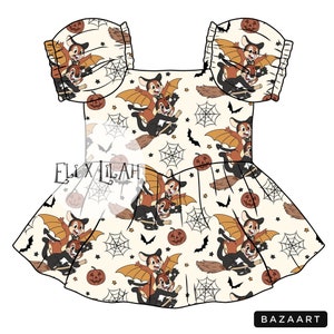 May include: A white dress with a cream background featuring a repeating pattern of cartoon squirrels flying on broomsticks with bats and spiderwebs. The dress has a ruffled bottom and short sleeves with ruffles.