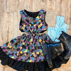 May include: A black and blue patchwork dress with a yellow and pink pattern. The dress has a cut-out design on the sides and a ruffled hem. The dress is paired with black boots and blue tights with a stitched design.