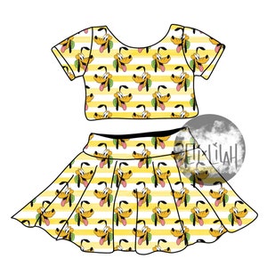 May include: A yellow and white striped crop top and skirt set with a cartoon dog print. The dog is wearing a green collar and has a tongue sticking out.