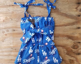 May include: A blue and white baby onesie with a pattern of baseballs and the words "LA Dodgers".