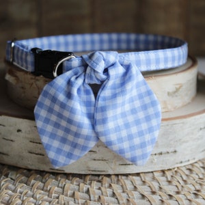 Puede incluir: Un collar de perro de cuadros azules y blancos con una pajarita. El collar est&aacute; sobre una superficie de madera.