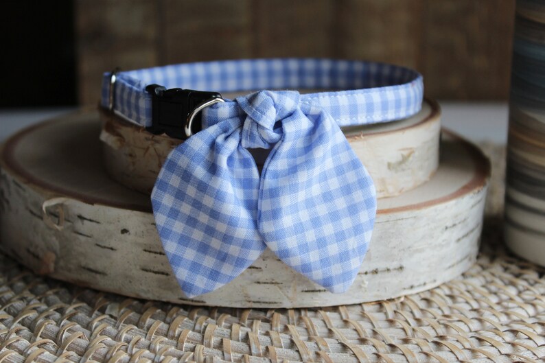 Puede incluir: Un collar de perro de cuadros azules y blancos con una pajarita. El collar est&aacute; sobre una superficie de madera.