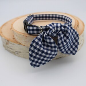 K&ouml;nnte beinhalten: Ein blaues und wei&szlig;es Gingham-Hundehalsband mit einer Schleife. Das Halsband liegt auf einer Holzoberfl&auml;che.