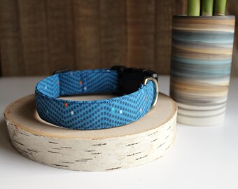 Puede incluir: Un collar de perro azul con un patrón de lunares blancos y naranjas. El collar está sobre una superficie de madera clara.