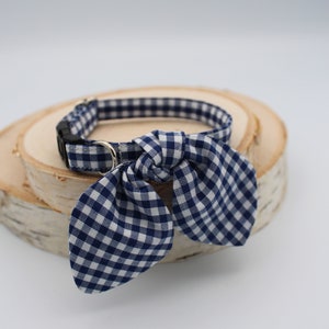 K&ouml;nnte beinhalten: Ein blaues und wei&szlig;es Gingham-Hundehalsband mit einer Schleife. Das Halsband liegt auf einer Holzoberfl&auml;che.
