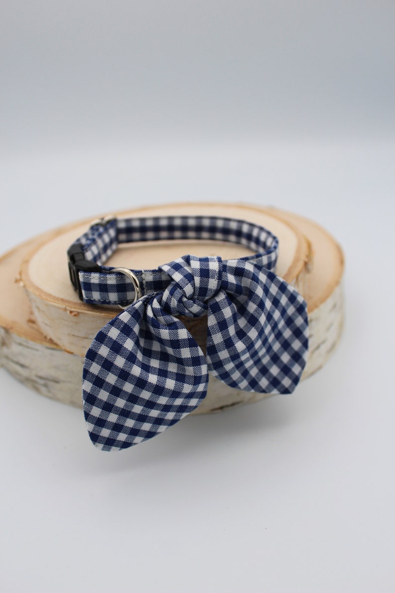 K&ouml;nnte beinhalten: Ein blaues und wei&szlig;es Gingham-Hundehalsband mit einer Schleife. Das Halsband liegt auf einer Holzoberfl&auml;che.