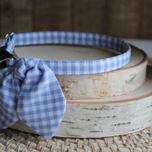 Puede incluir: Un collar de perro de cuadros azules y blancos con una pajarita. El collar est&aacute; sobre una superficie de madera.