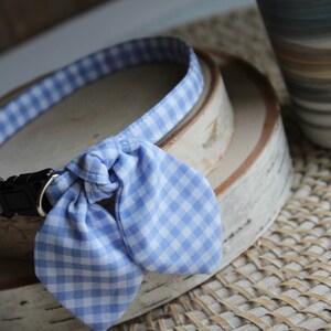 Puede incluir: Un collar de perro de gingham azul y blanco con una pajarita. El collar est&aacute; sobre una superficie de madera.