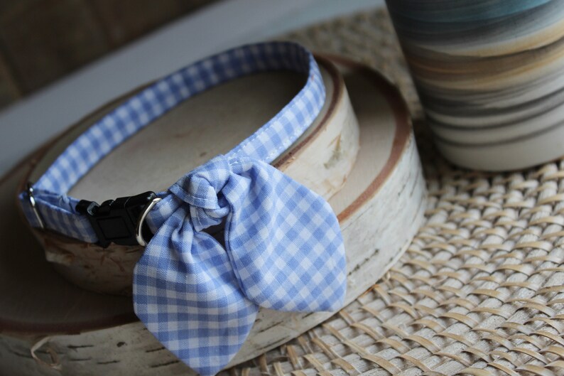 Puede incluir: Un collar de perro de gingham azul y blanco con una pajarita. El collar est&aacute; sobre una superficie de madera.