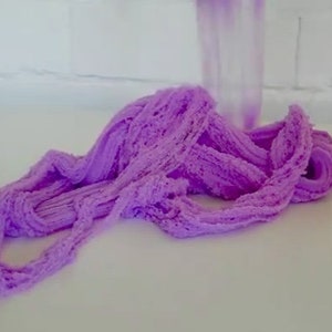 May include: Purple slime with a textured, fluffy appearance. The slime is piled in a mound on a white surface.