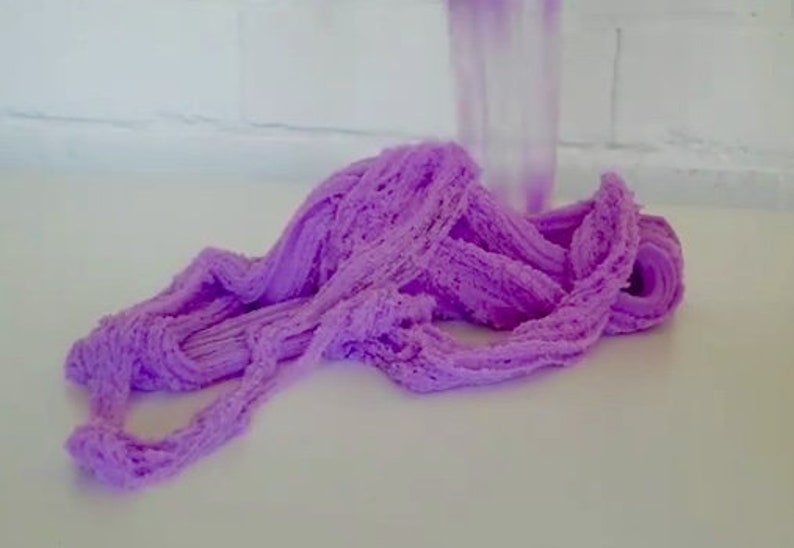 May include: Purple slime with a textured, fluffy appearance. The slime is piled in a mound on a white surface.