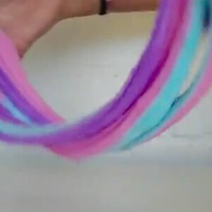 May include: A close-up of a multi-colored slime being stretched and pulled. The slime is pink, purple, and blue.