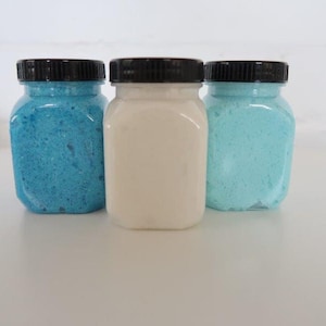 May include: Three glass jars with black lids filled with blue, white, and light blue bath salts.