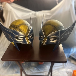 May include: Two yellow and blue Wolverine helmets with a distressed paint finish. The helmets have a textured surface and are made of a hard plastic.