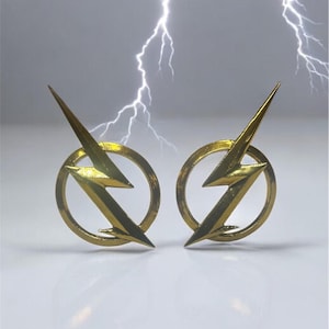 May include: A pair of gold-coloured lightning bolt earrings. Each earring has a lightning bolt design within a circular frame. The background shows a grey sky with white lightning bolts.