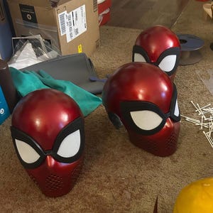 Peut inclure: Plusieurs masques de super-héros rouges et noirs avec des formes d'yeux blancs sont disposés sur une surface. Les masques ont une finition brillante et une zone texturée autour de la bouche. Ces masques sont probablement destinés au cosplay ou aux costumes.