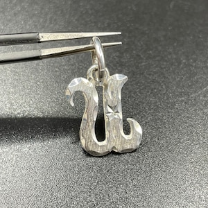May include: Silver charm in the shape of the letter U. The charm has a textured, diamond-like pattern.