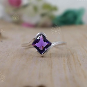 Peut inclure: Une bague en argent avec une pierre précieuse améthyste de forme carrée. La bague a un design de bande torsadée.