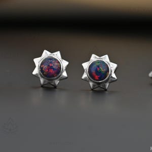 Op de afbeelding: Een paar zilveren oorknopjes met een ronde, donkere opaal cabochon gezet in een zonnestraalvormig montuur. De metalen achterkantjes zijn duidelijk gestempeld met 925, wat duidt op een samenstelling van sterling zilver.