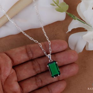 Op de afbeelding: Een zilveren ketting met een rechthoekige, smaragdgroene edelsteen hanger. De hanger is gezet in een zilveren montuur en hangt aan een fijne zilveren ketting. De ketting wordt getoond tegen een neutrale achtergrond.