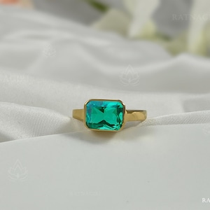Pode incluir: Um anel de ouro com uma grande gema verde esmeralda. O anel é engastado em uma simples moldura quadrada.