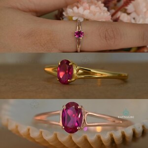 May include: A gold and rose gold ring with a large oval ruby gemstone. The ring is shown in three different views, including one on a finger and another resting on a seashell.