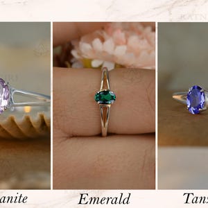 May include: Three rings with oval gemstones: morganite, emerald, and tanzanite. Each ring has a silver band. The morganite ring is light pink, the emerald ring is green, and the tanzanite ring is blue. The word "Morganite", "Emerald", and "Tanzanite" are written below each ring.