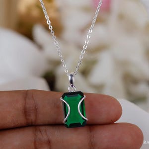 以下が含まれることがあります： 長方形のエメラルドグリーンのペンダントが付いたシルバーのネックレス。ペンダントは、曲線的なアクセントが付いたシルバーフレームにセットされています。チェーンは繊細で、ペンダントがジュエリーの焦点となっています。