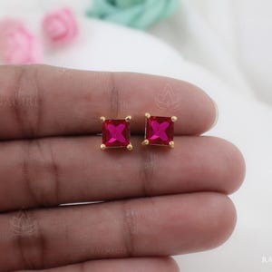 May include: A pair of gold stud earrings with square-shaped red gemstones.