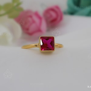 May include: A gold ring with a square-shaped, bright pink gemstone.