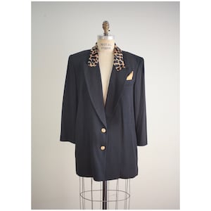 Könnte beinhalten: Ein schwarzer Blazer mit langer, überdimensionierter Passform. Der Blazer hat einen Kragen mit Leopardenmuster und goldene Knöpfe.