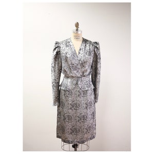 May include: A gray and white floral print dress with a fitted bodice and a slightly flared skirt. The dress has a V-neckline and long sleeves with puffed shoulders.