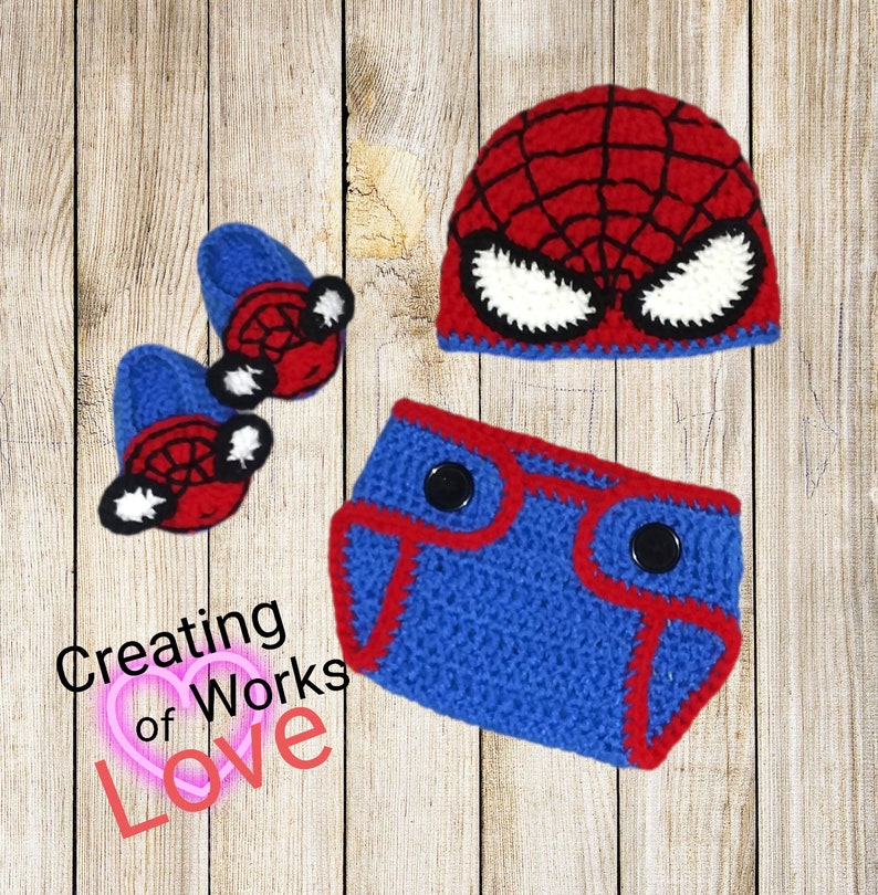 Puede incluir: Un conjunto de beb&eacute; de ganchillo en rojo, azul y blanco con un dise&ntilde;o de Spiderman. El conjunto incluye un gorro, una cubierta de pa&ntilde;al y botines.