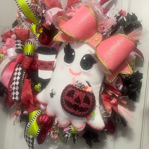 May include: A Halloween wreath featuring a white ghost with a pink bow and a jack-o'-lantern. The wreath is decorated with ribbons in black, pink, red, and green, and includes a coffee cup and other festive elements.