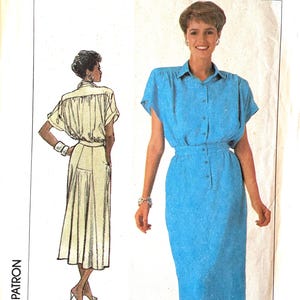 May include: A Simplicity sewing pattern envelope featuring a bright blue dress with a collared neckline, short sleeves, and a button-down front. The illustration shows a front view of the dress on a model and a back view sketch of the garment.