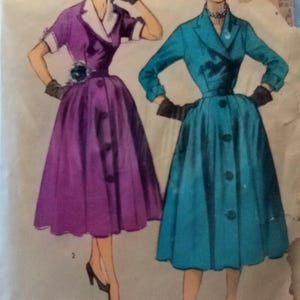 Puede incluir: Un sobre de patrón de costura vintage con ilustraciones de dos vestidos. Uno es un vestido morado de manga corta con cuello blanco, y el otro es un vestido azul verdoso de manga larga con cuello de solapa. Ambos vestidos tienen botones y faldas amplias.