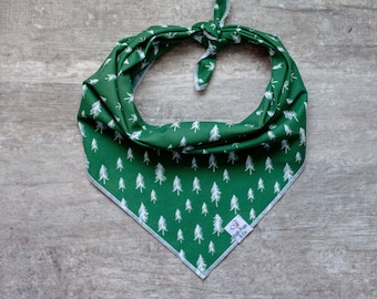 May include: A green dog bandana with a white tree pattern. The bandana is tied at the top and has a white border. The bottom corner has a small white tag with the text "Trash Pups & Co."