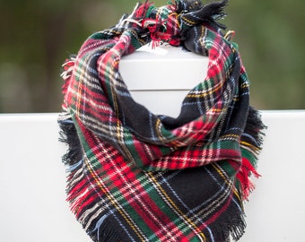 May include: A black, red, and green plaid bandana with frayed edges. The bandana is tied in a knot and is hanging on a white fence.