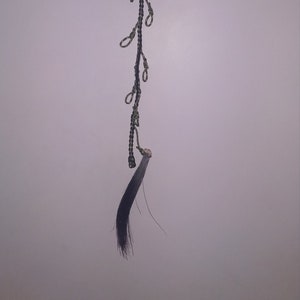 May include: A black and green braided cord with multiple loops hanging from it. The cord is attached to a black horsehair tassel.