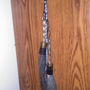 May include: A black and white braided cord with two shotgun shell tassels hanging from it. The cord is attached to a metal ring at the top.