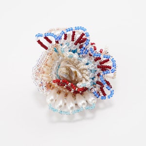 May include: A beaded flower brooch with a shell center, featuring red, blue, and white beads.