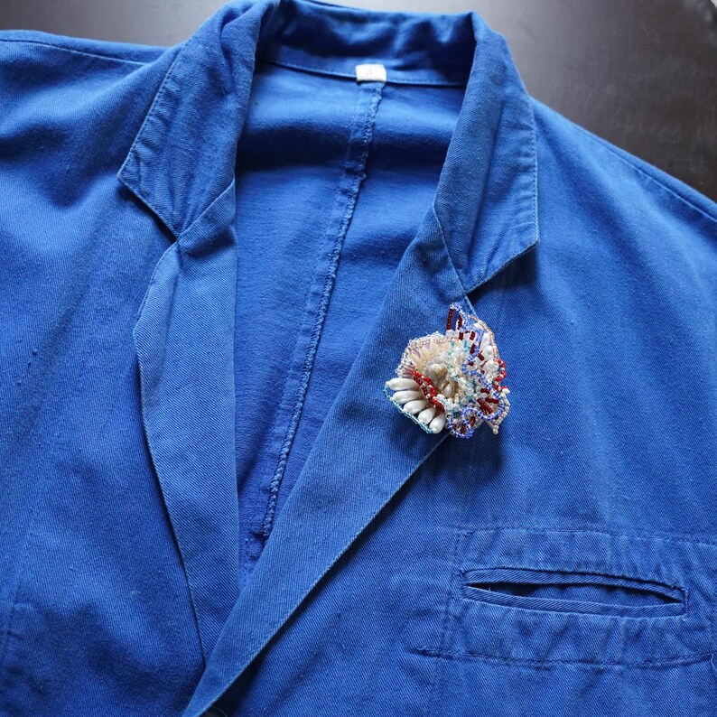 May include: A blue denim jacket with a colorful beaded flower brooch pinned to the lapel.