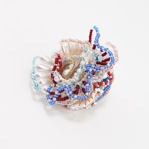 May include: A cluster of iridescent beads in shades of blue, red, and white, with a pearl-like center. The beads are arranged in a swirling, organic pattern, creating a unique and eye-catching piece of jewelry.