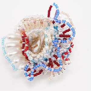 May include: A close-up of a beaded flower brooch with a pearl-like center and red, blue, and white beads.