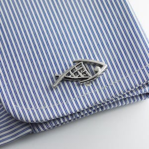 May include: Silver cufflinks in the shape of a stylized fish. The cufflinks are on a blue and white striped shirt.